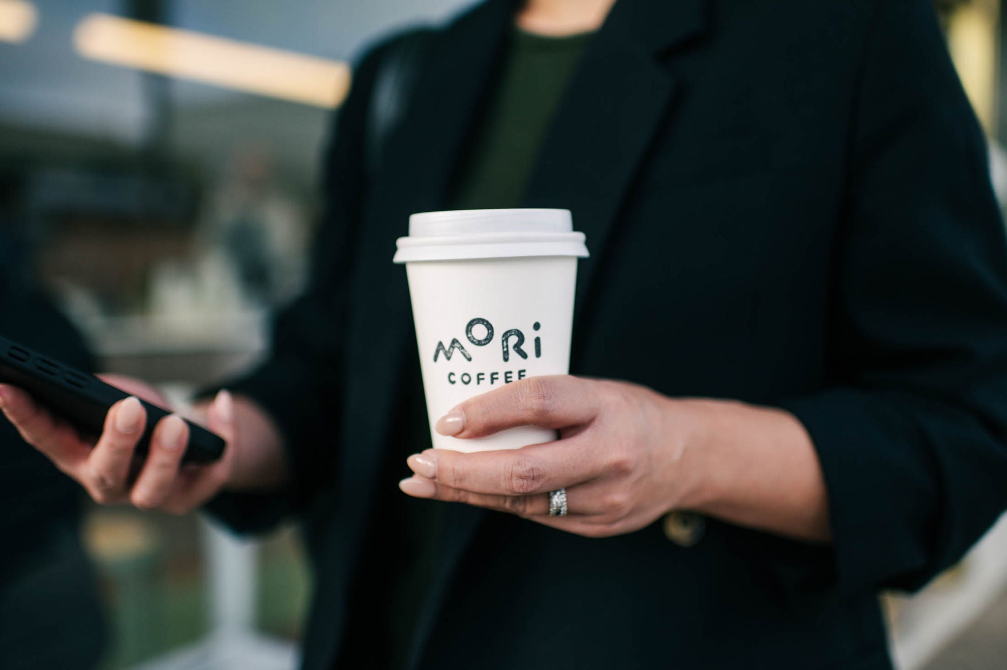 Person holding a white coffee cup with 'Mori Coffee' branding.